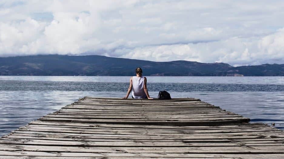 A woman sitting on a dock overlooking a lake and mountains.