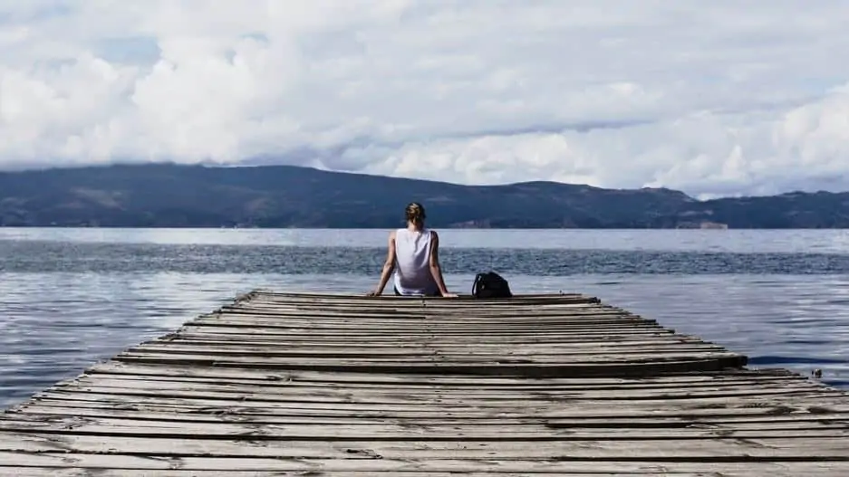 A woman sitting on a dock overlooking a lake and mountains.