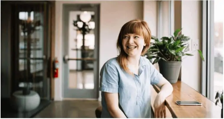 A mom sitting by a window smiling.