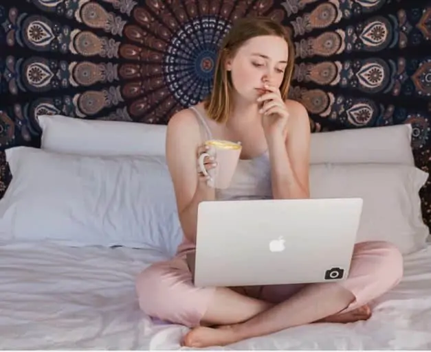 A woman sitting on her bed working on a research study on her laptop