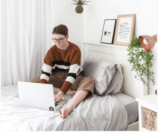 woman sitting on her bed working on her laptop tutoring online 