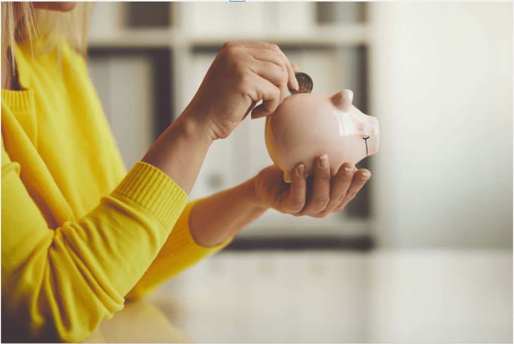 Women wearing yellow shirt putting coins into a piggy bank.