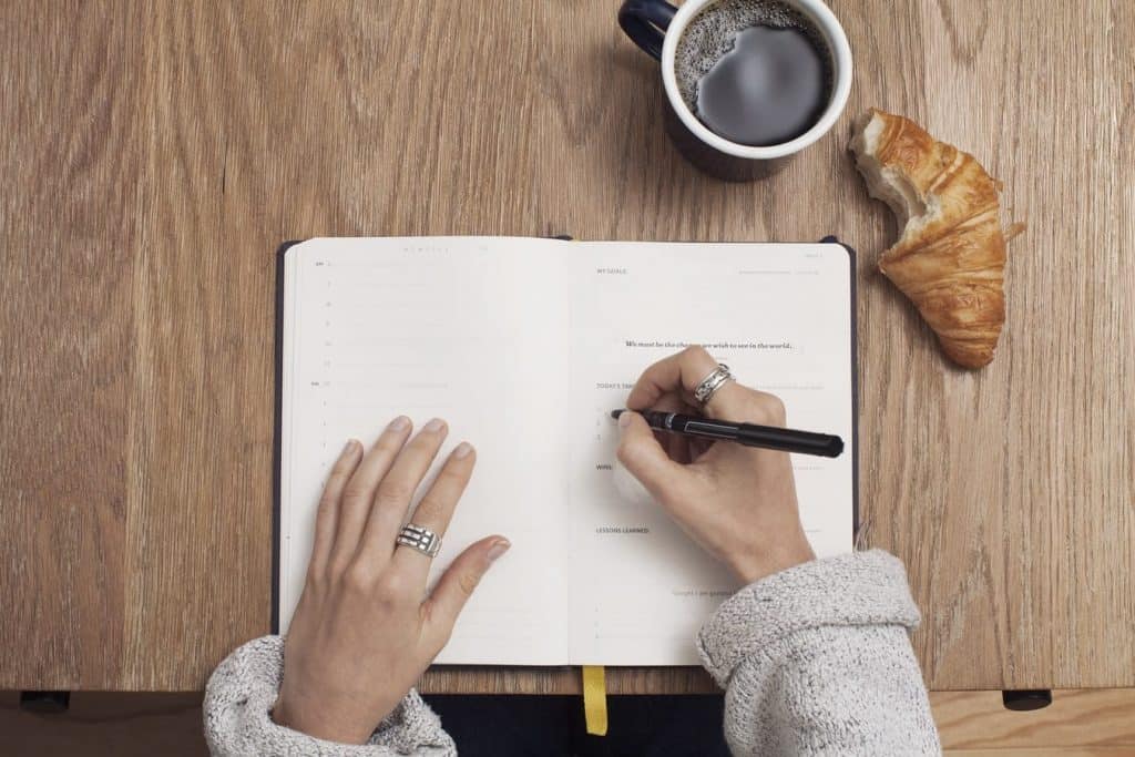 A woman writing her goals in a notebook while eating breakfast