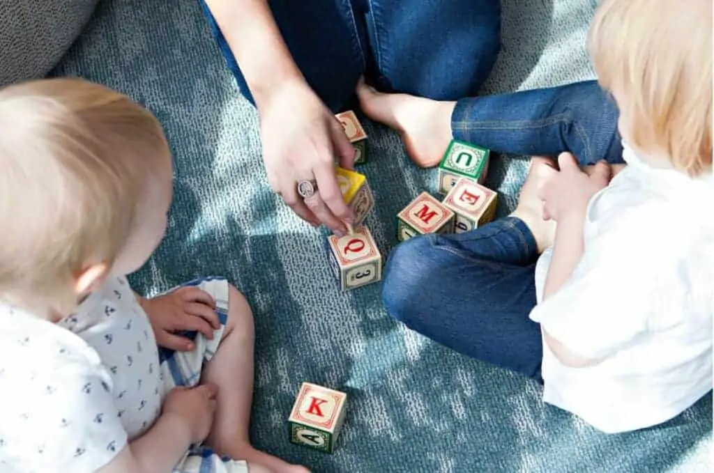 woman babysitting two children and playing blocks