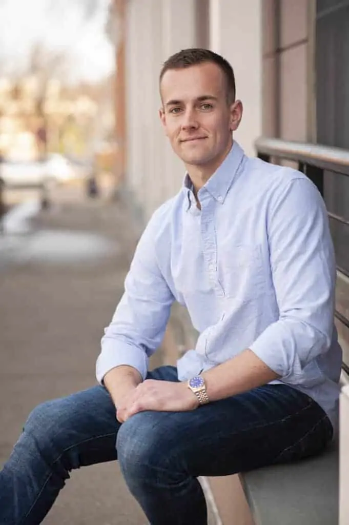 A man in a light blue button up smiling, posing for a picture