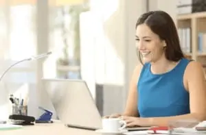 A woman wearing a blue shirt working from home on her laptop