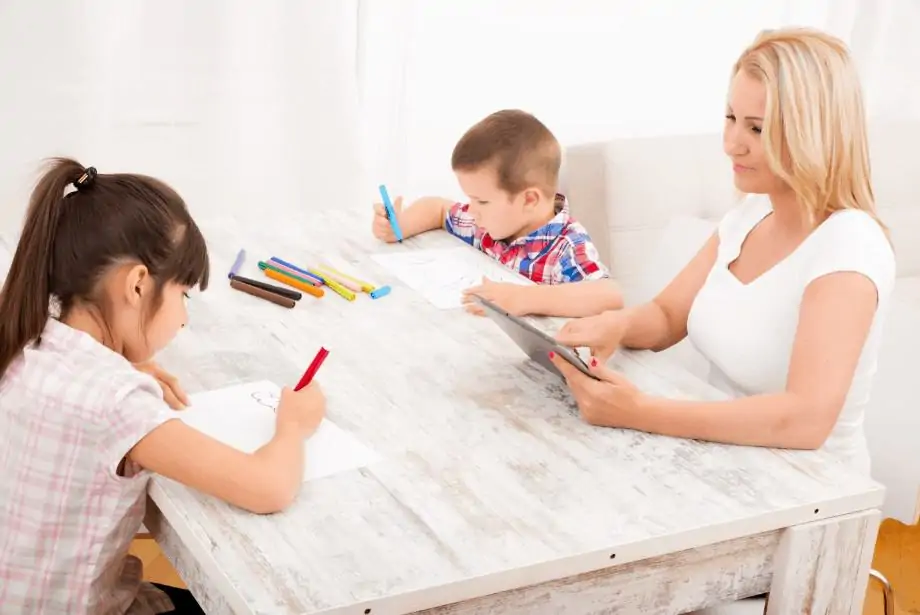 Une maman travaille sur un ordinateur portable pendant que ses enfants colorient des images à ses côtés