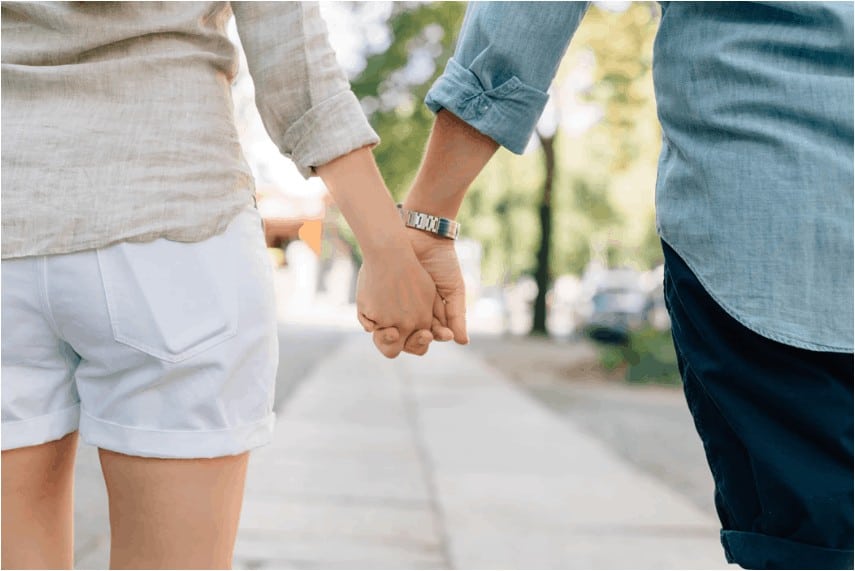 A man and woman walking, holding hands.
