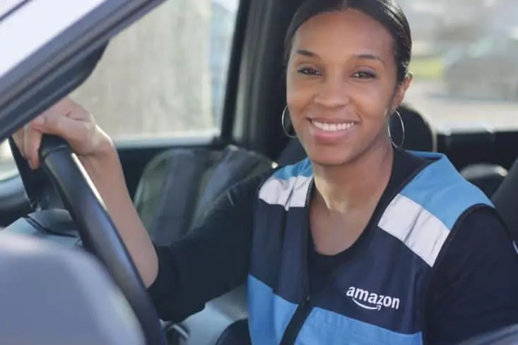 A woman sitting in a Amazon van, making deliveries.