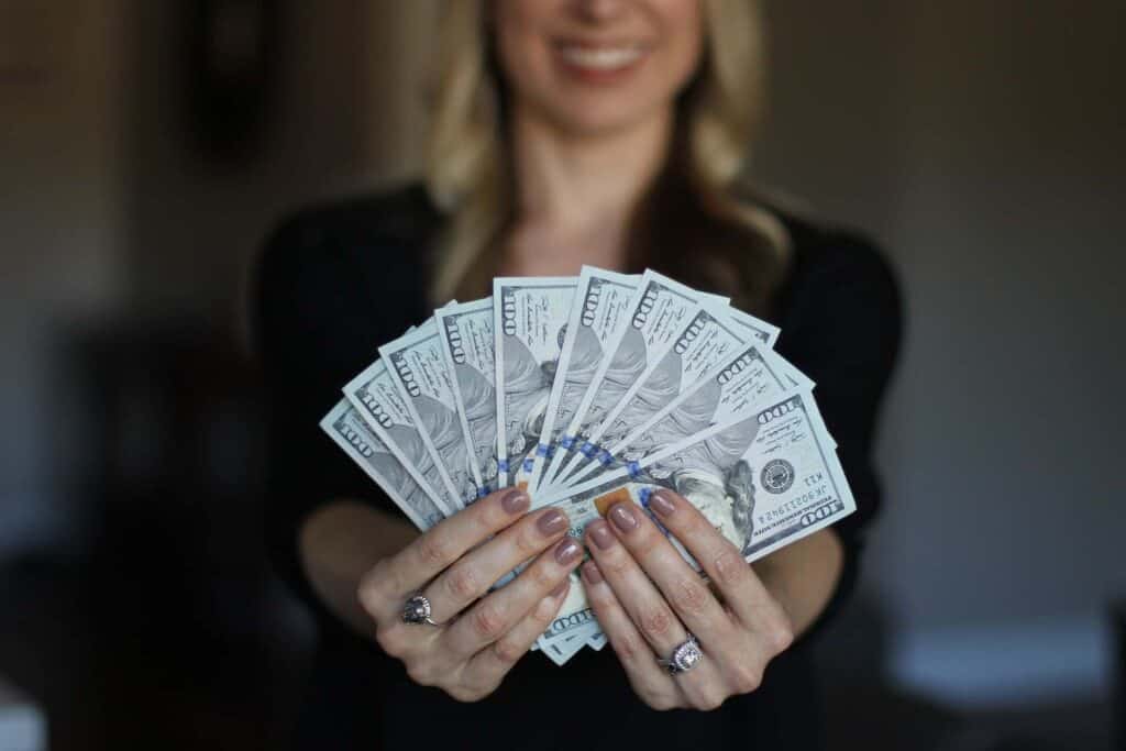 A woman holding ten $100 dollar bills