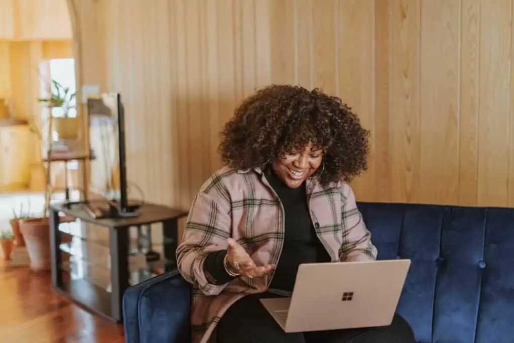 A woman sitting on a blue couch with her laptop.  She is selling her used items online.