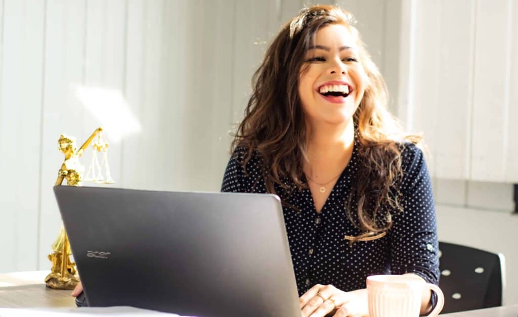 A woman in a black polka dot shirt smiling while working on her laptop