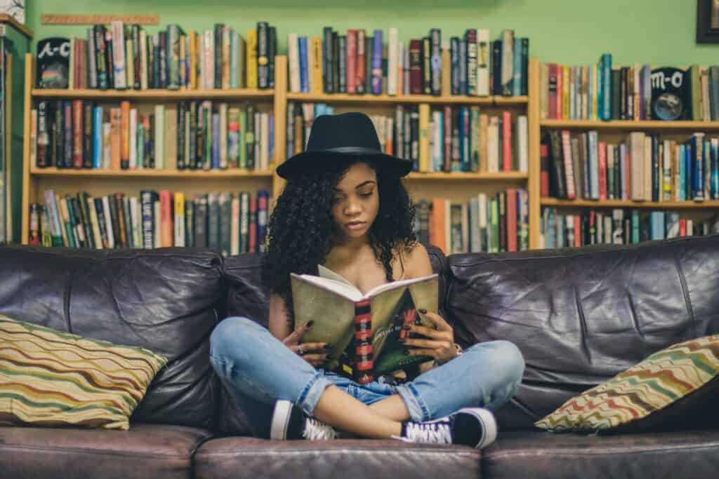 A woman sitting on a couch reading a book in front of a huge bookshelf