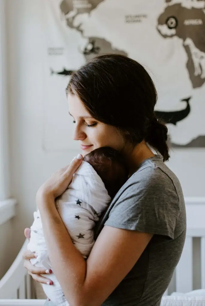 A woman holding a sleeping baby wrapped in a blanket